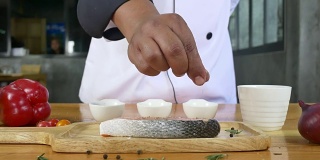 近距离美食厨师或厨师调味新鲜块熟食块鲑鱼与海盐和磨碎的辣椒。