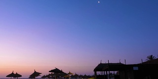 一弯新月撑着稻草伞在海滩上美丽的夜空上