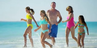 一个白人家庭穿着五颜六色的泳衣赤脚在海滩上