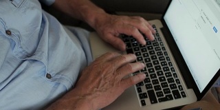 动态视频。摄影机过来了。一个退休的手用电脑键盘工作的特写。网上银行，笔记本电脑，现代电子产品和退休年龄的人