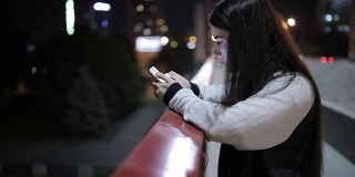 年轻女子晚上站在桥上使用智能手机应用