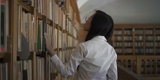 年轻的亚洲女研究员在书架上寻找一本书