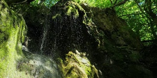 慢镜头，瀑布在山上高速卷。特写的春天的水滴下落和溅在绿色的苔藓