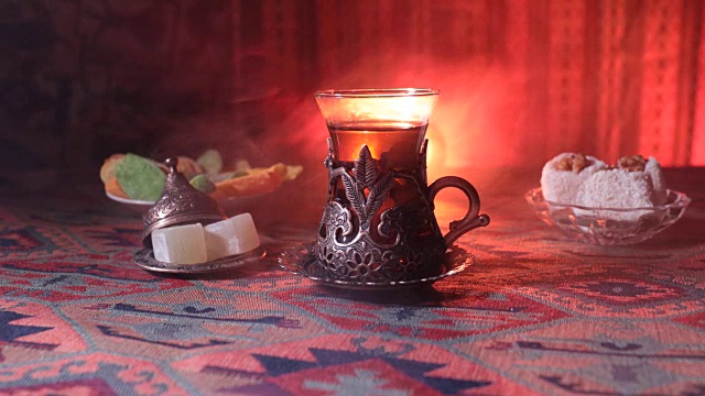 用复古玻璃杯盛着阿拉伯茶，地毯上放着东方小吃。东方茶道在黑暗的背景与灯光和烟雾。空的空间。有选择性的重点。滑块拍摄