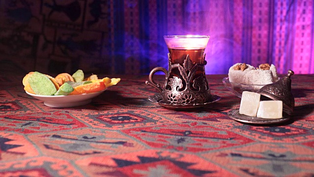 用复古玻璃杯盛着阿拉伯茶，地毯上放着东方小吃。东方茶道在黑暗的背景与灯光和烟雾。空的空间。有选择性的重点。滑块拍摄