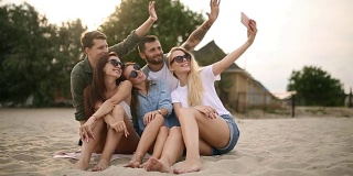一群年轻的朋友在海滩上自拍。在温暖的夏夜，男男女女坐在沙滩上拍照