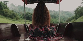 时髦的女人坐在船甲板上，旅行到河边的绿色区域的森林