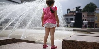 美丽的小女孩站在城市喷泉旁