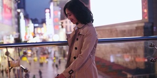 侧面的一个漂亮的快乐年轻的亚洲女人走在城市的街道在晚上与手机在手摇慢动作