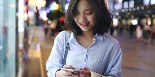 一个漂亮的年轻亚洲女人在晚上使用智能手机的慢动作特写