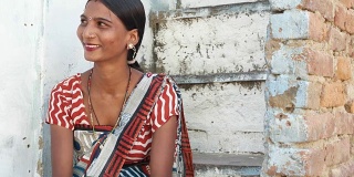 年轻漂亮的女人在家里四处寻找建议，困惑的笑声，微笑，疑惑的微笑坐在台阶上，穿着传统的印度次大陆纱丽连衣裙和衬衫