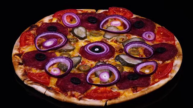 美味的自制披萨，配有泡菜、意大利腊肠、番茄、橄榄、奶酪和洋葱圈，在黑色背景上旋转