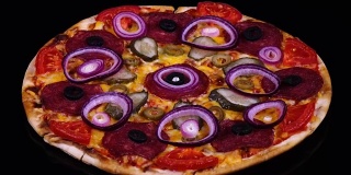 美味的自制披萨，配有泡菜、意大利腊肠、番茄、橄榄、奶酪和洋葱圈，在黑色背景上旋转
