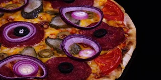 色彩缤纷的自制披萨，配有从烤箱中取出的泡菜和洋葱，在黑色背景下旋转