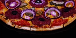 美味的自制披萨与泡菜和洋葱刚从烤箱旋转的黑色背景