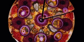 用意大利腊肠、泡菜、橄榄、西红柿、奶酪和洋葱圈烤出来的自制披萨，在黑色背景上旋转着切下来的披萨