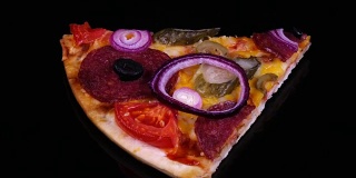一块自制的披萨，配上腌黄瓜和洋葱，在黑色的背景下旋转