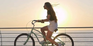 年轻迷人的女人骑着老式自行车在海边日出或日落