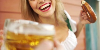 酒醉了，一个年轻的女孩在十月啤酒节上喝着啤酒，她非常高兴，笑得很大声。穿着巴伐利亚服装