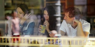 一个男人和两个了不起的女人在咖啡馆喝鸡尾酒。透过餐厅的窗户看到三个朋友