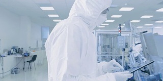 科学家使用数字平板电脑和穿着防护服走过制造实验室与现代工业机械。产品制造工艺:制药，半导体，生物技术。