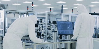 在实验室，科学家穿着防护服做研究，使用显微镜和输入数据到个人电脑。现代制造半导体和制药项目。