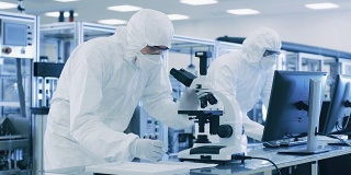 在实验室，科学家穿着防护服做研究，使用显微镜和输入数据到个人电脑。现代制造半导体和制药项目。