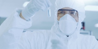 在实验室研究员/科学家穿着防护服拿着装有实验药物的试管并看着它。