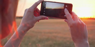 年轻的女人用手机拍日落的特写