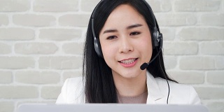 美丽的亚洲女接线员戴着麦克风在呼叫中心与客户交谈