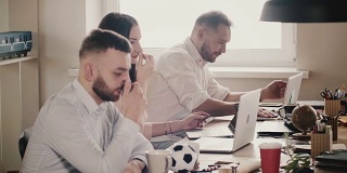 快乐的年轻欧洲商人坐在桌边，在现代健康的办公室里与笔记本电脑一起工作，慢镜头