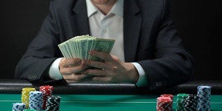 赌场的幸运赢家手里拿着美元钞票，桌上摆着筹码，游戏奖励
