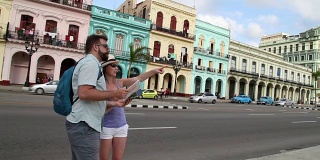 在古巴哈瓦那，游客在首都主干道附近看地图寻找方向，路上有过路的人和汽车