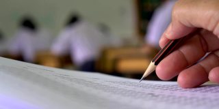 教育考试概念:高中课堂上，学生手持考笔，写答题卡或练习题，在木桌上用复写纸电脑答题