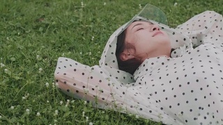 穿着雨衣睡在草地上的漂亮女人视频素材模板下载