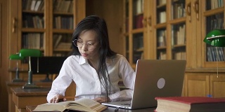勤奋的女学生生物学家在桌子上写书和笔记本电脑在图书馆