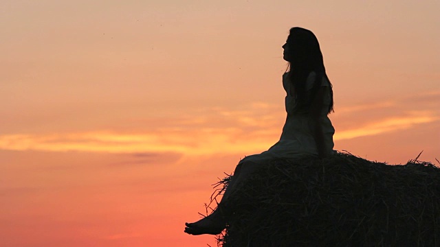 美丽的女人剪影坐在草球欣赏自然日落