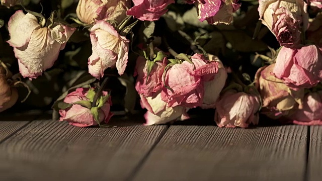 木桌上放着一束枯萎的玫瑰花。干粉色奶油黄色玫瑰