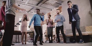 在现代办公室的慢动作中，多民族商务人士在团队建设的非正式舞会上庆祝商业成功