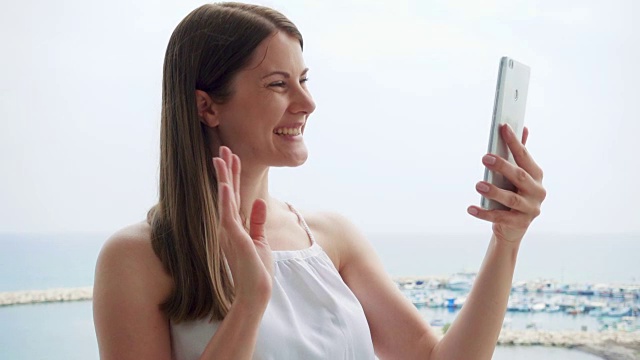度假的女人在阳台上通过手机messenger应用程序与朋友视频聊天的慢动作