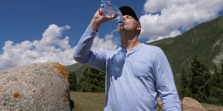 戴着帽子的人在山上喝着瓶子里的水，背景是蓝天
