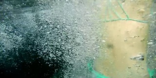 一个穿着绿松石泳衣的年轻女子跳入水中，有很多泡泡