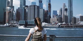 快乐的女游客背双肩包举起双臂，在纽约的天际线，看回相机