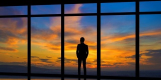 在日出的背景下，站在窗边的男人。时间流逝