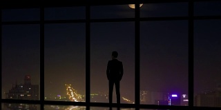 这名男子站在城市夜景的全景窗旁