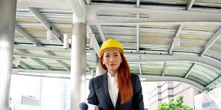 年轻貌美的亚洲工程师，穿着西装，戴着安全帽，走在办公楼的通道上