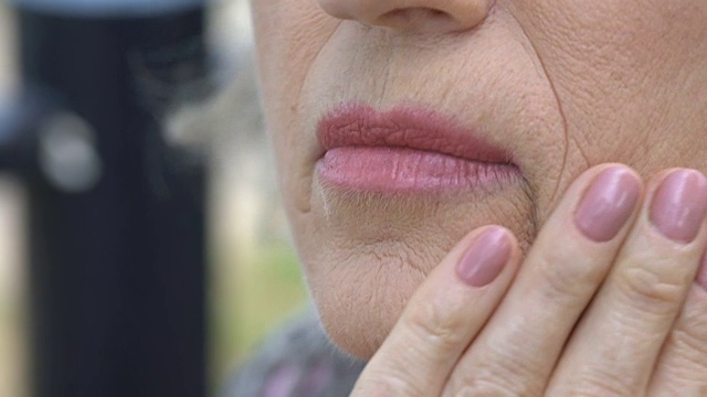 老年妇女抚摸着她布满皱纹的脸庞，皮肤老化的过程，渴望年轻