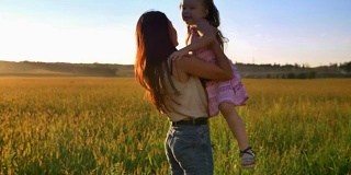 母亲抱起女儿的剪影，带着孩子在夏天的田野里散步，家庭观念