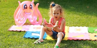 小女孩吃了一个西瓜。宝宝在夏天吃东西。野餐在绿色的草地或草坪上