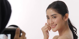 在幕后的美丽的年轻亚洲女性模特美丽的脸和完美的皮肤被记录在一个摄像机在一个白色的背景。